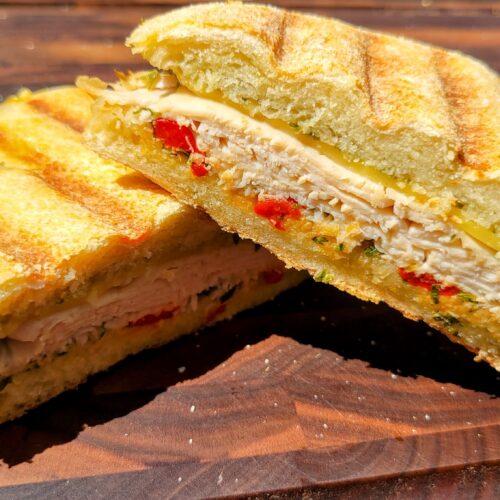 Turkey pesto and roasted red pepper panini on wooden cutting board